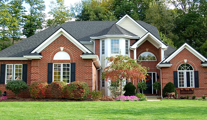 A large, two-story red brick suburban home with a gray shingle roof