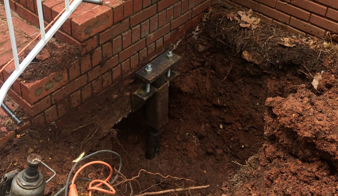 Metal support system installed during foundation repair due to soil settlement next to a brick wall