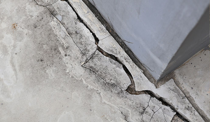 Large crack visible in a concrete floor close to the base of an interior wall