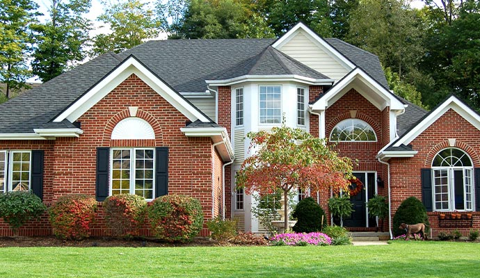 The front exterior of a large, well-manicured brick house with professional landscaping