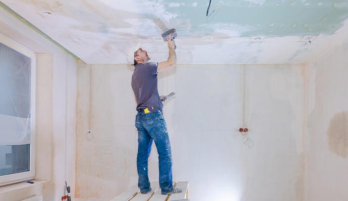 A worker applying fresh plaster to an interior ceiling during a home renovation