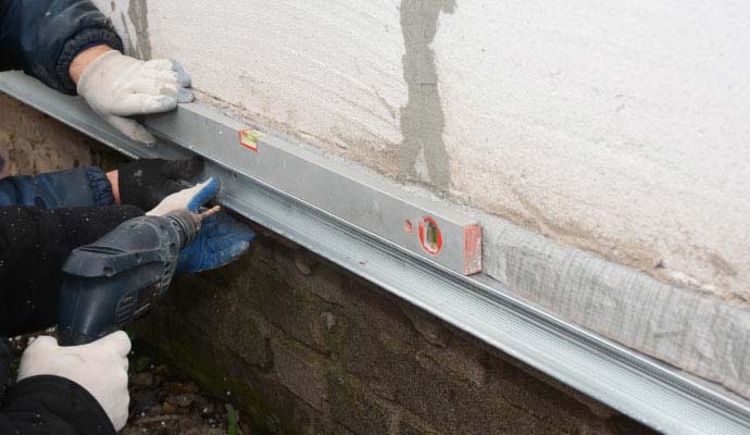 Technicians carefully repairing and strengthening an exterior foundation wall